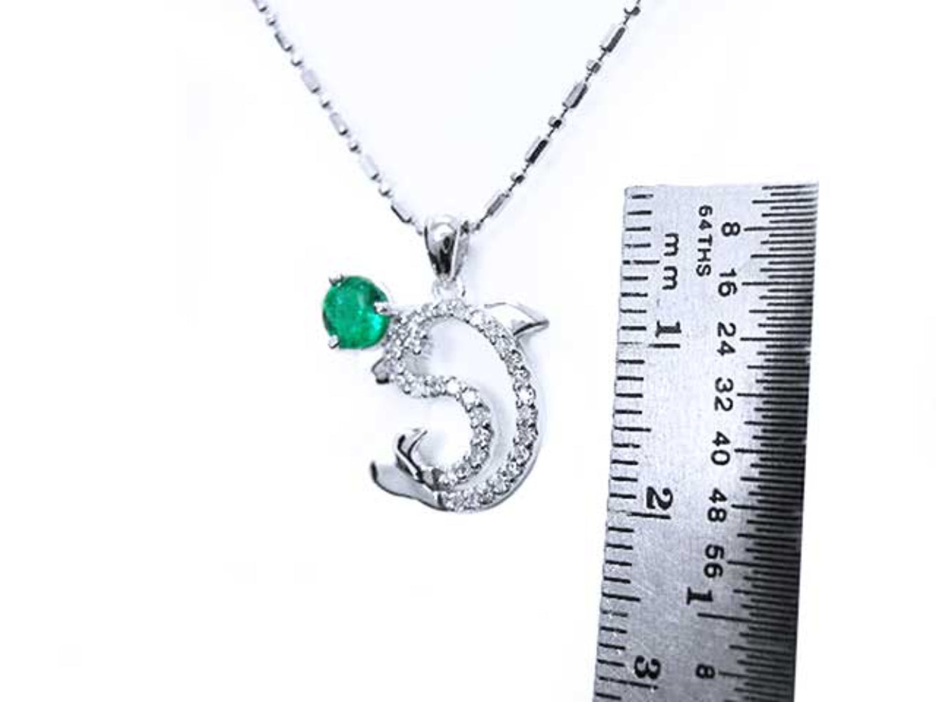 A Colombian emerald dolphin pendant next to a ruler on a white background
