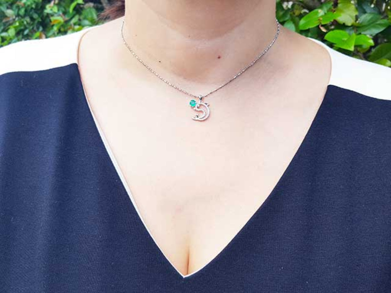 A woman wearing a Colombian emerald dolphin pendants pendant on a blue top.