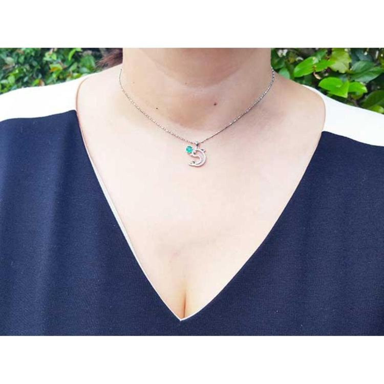 14K white gold dolphin pendant necklace with a deep green emerald, worn on a model.