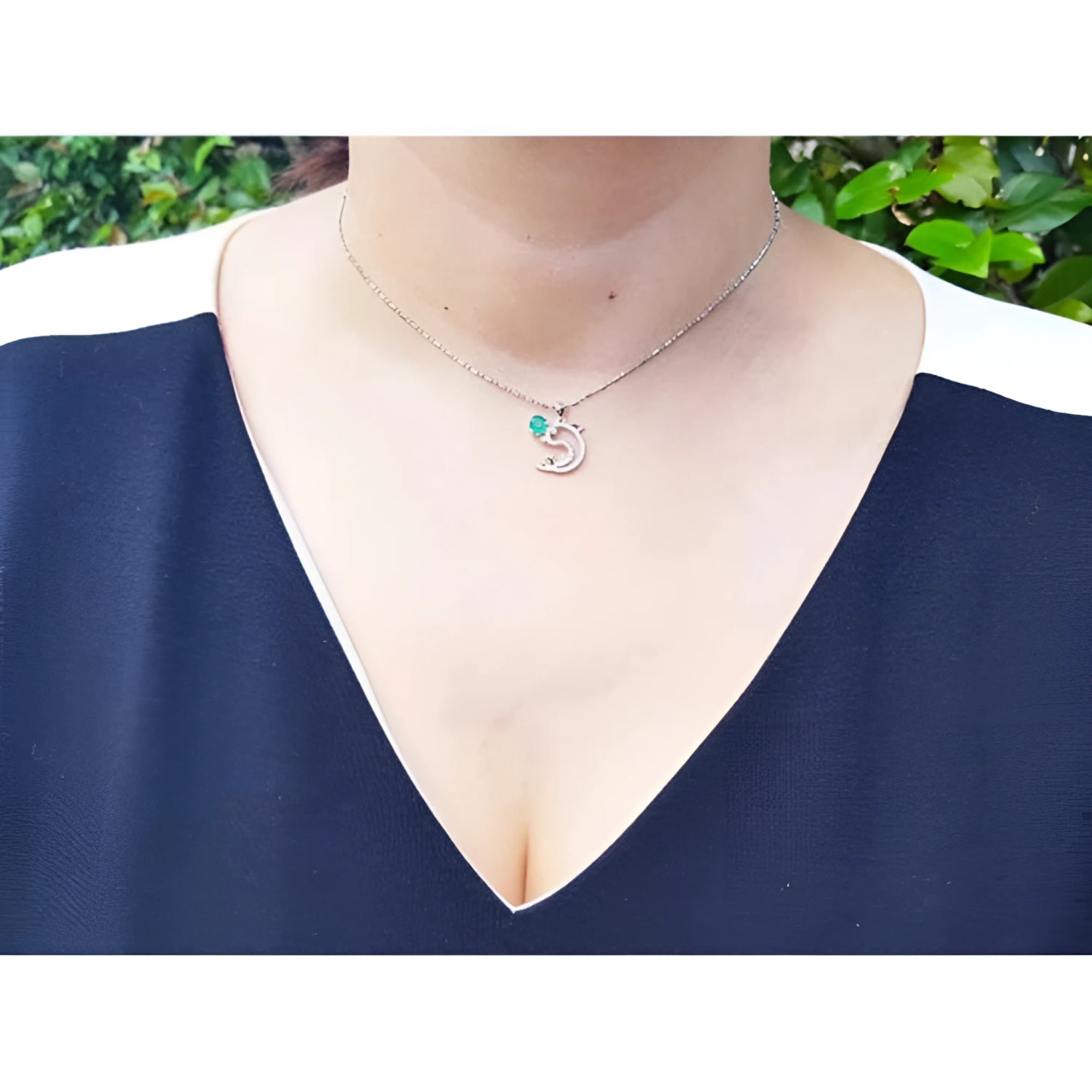 14K white gold dolphin pendant necklace with a deep green emerald, worn on a model.
