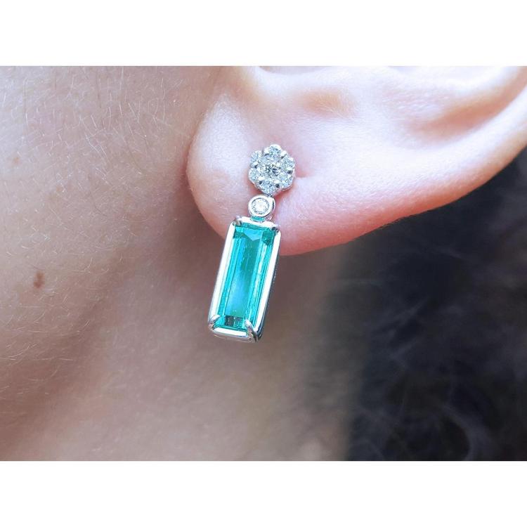 Close-up of a diamond and emerald earring on an ear with a blurred background