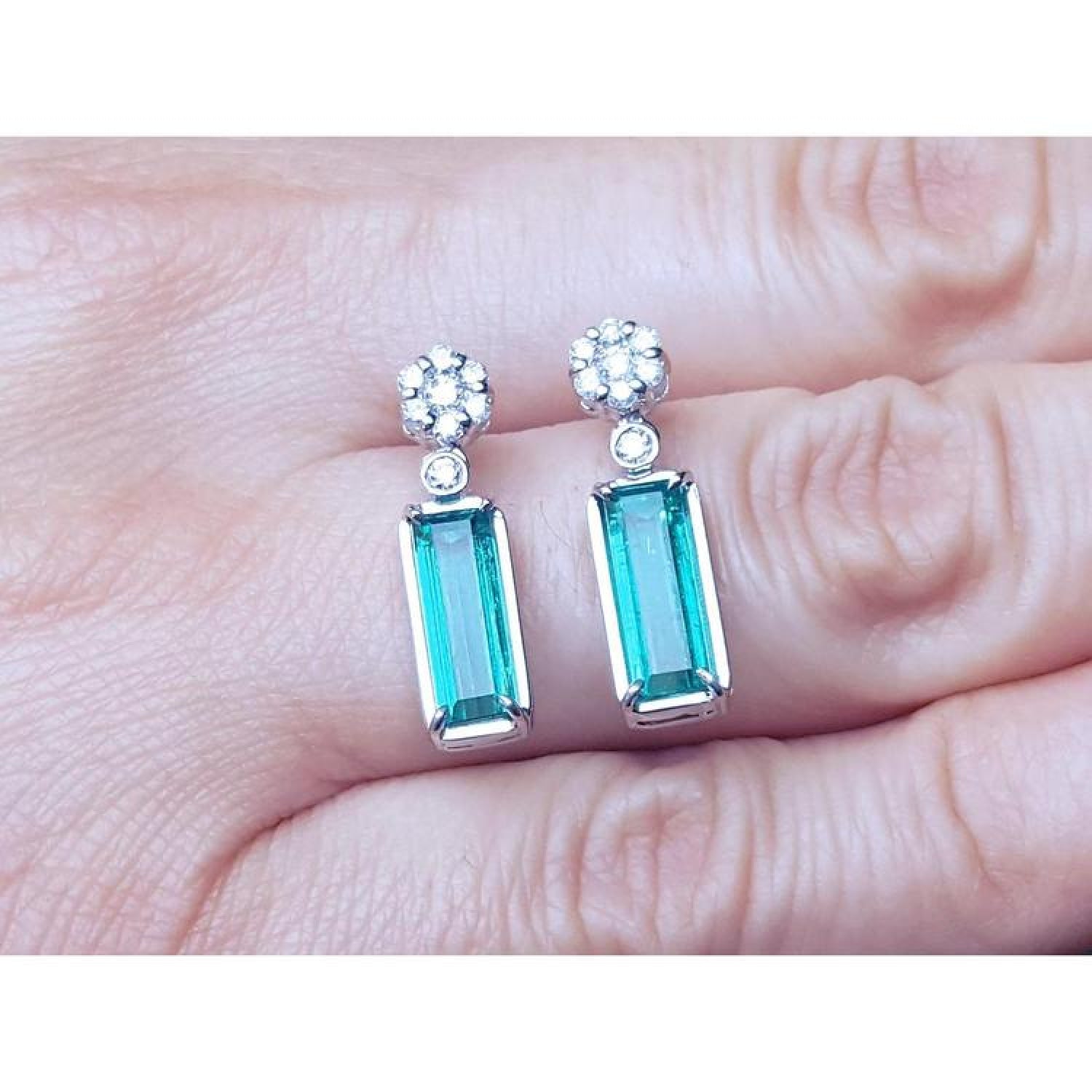 14K white gold dangling earrings with rectangular emeralds and diamond clusters.