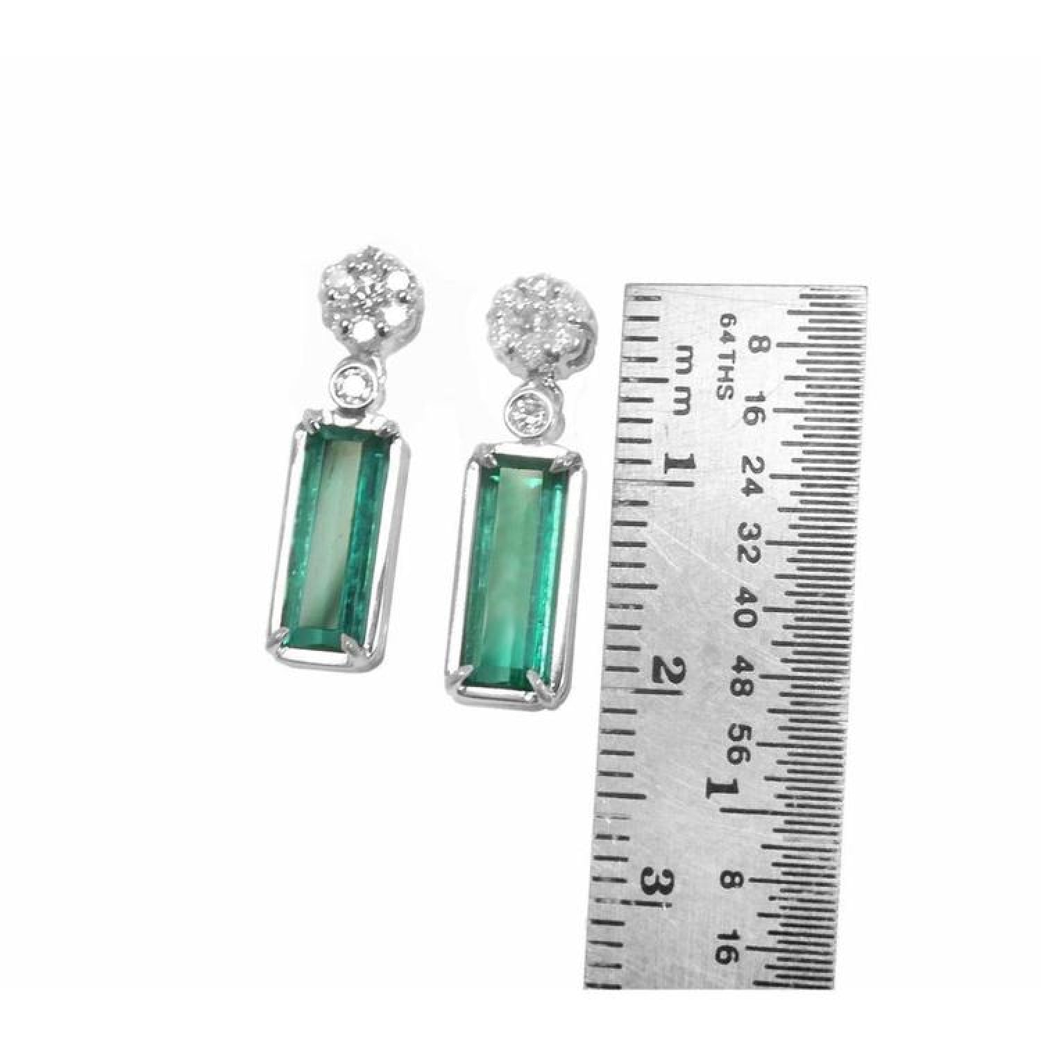 14K white gold dangling earrings with rectangular emeralds and diamond clusters, shown with a ruler.