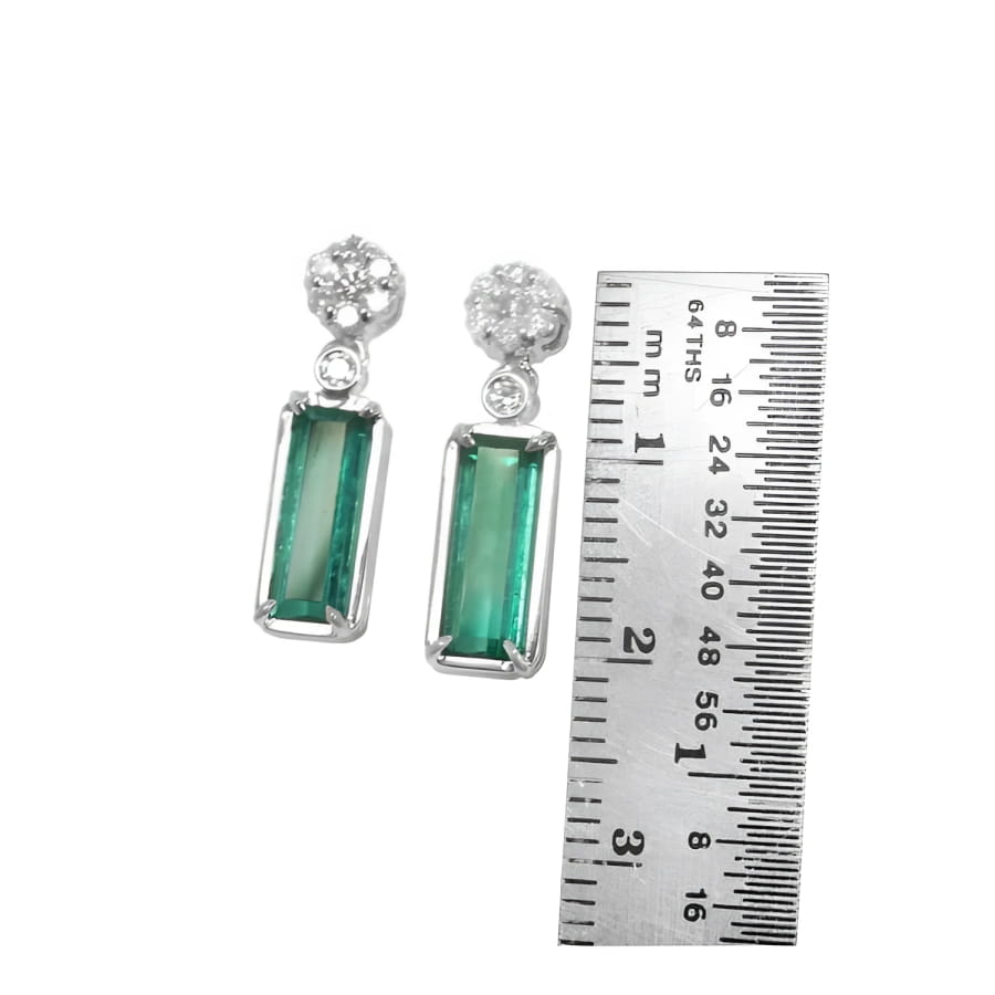 14K white gold dangling earrings with rectangular emeralds and diamond clusters, shown with a ruler.