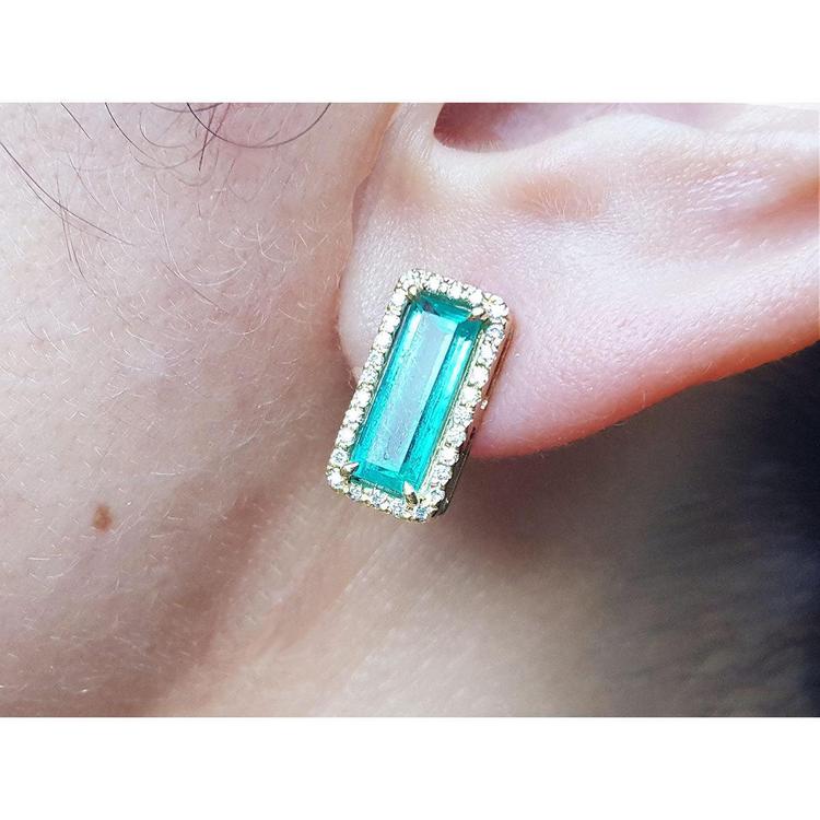 Natural emerald gemstone stud earring halo diamond 18k yellow gold worn on a person's ear.
