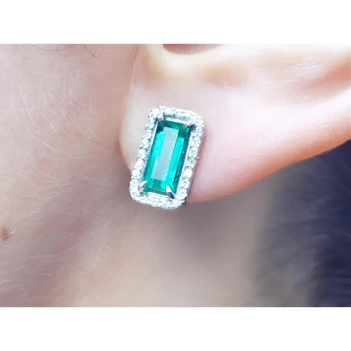 An emerald earring with halo diamond in 18k white gold on a earlobe