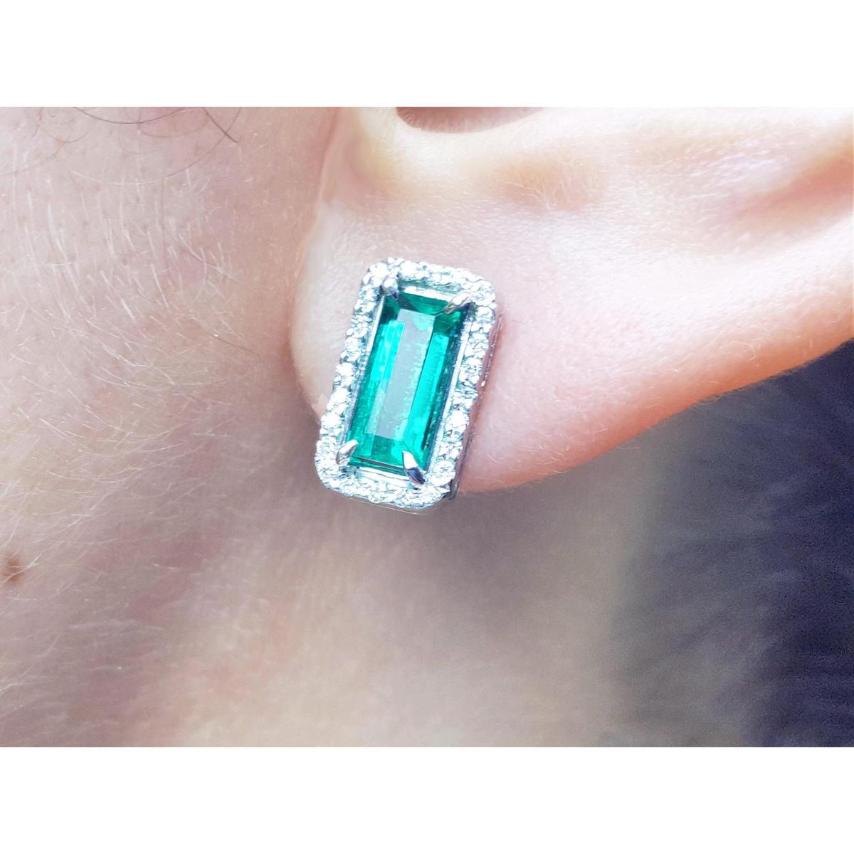 close up of an emerald earring with halo diamond in white gold on a earlobe