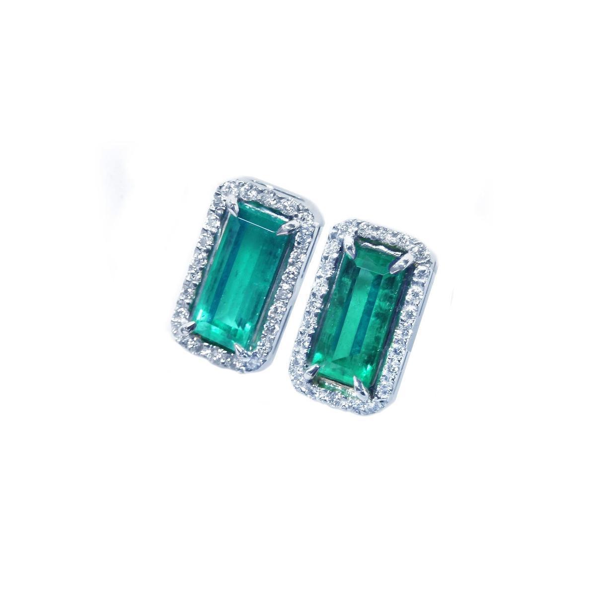 Pair of emerald earrings with halo diamond accents on a white background