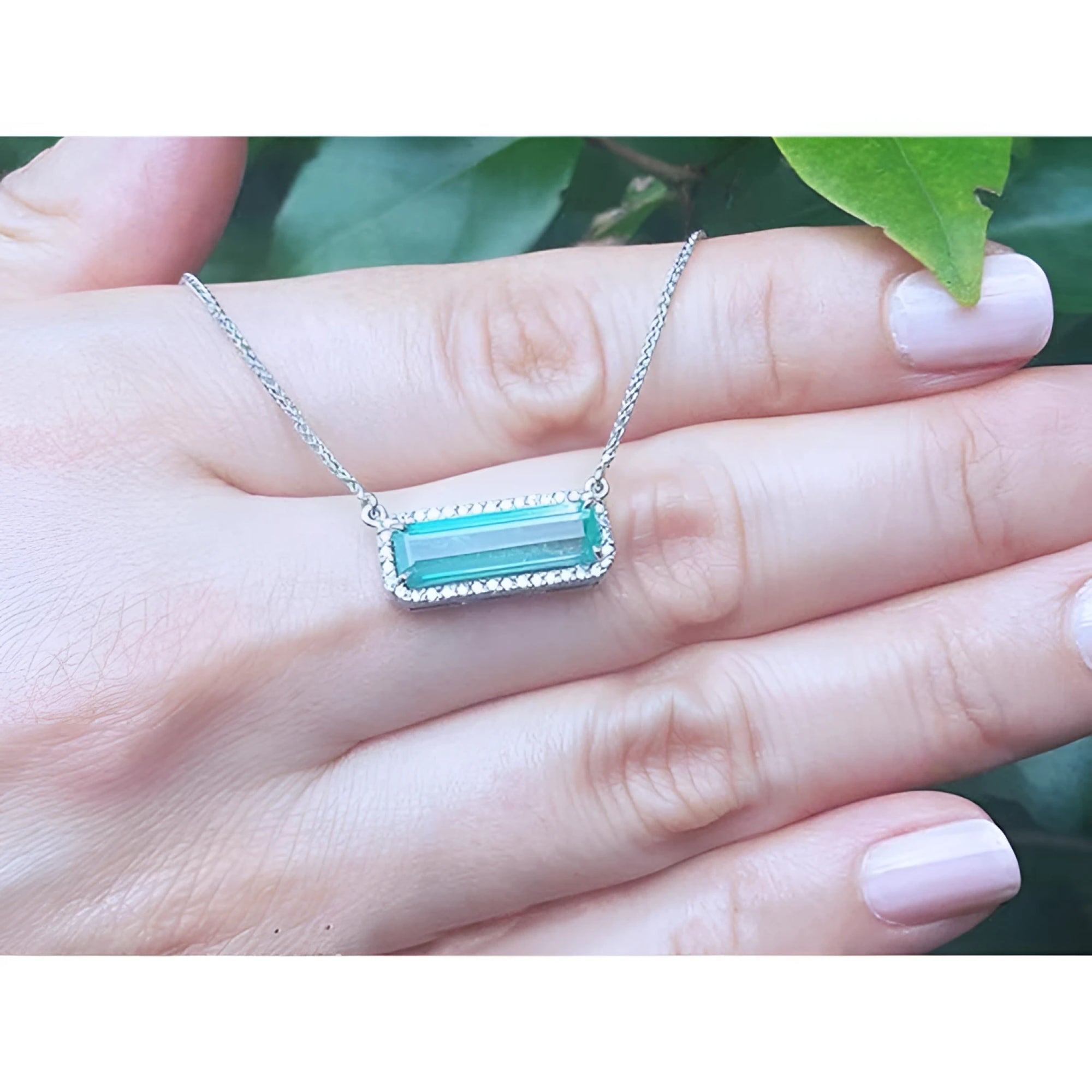 18K white gold necklace with a rectangular Colombian emerald and halo diamonds in an East-West design.
