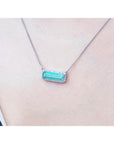 18K white gold necklace with a rectangular emerald-cut Colombian emerald and diamond halo, East-West design.