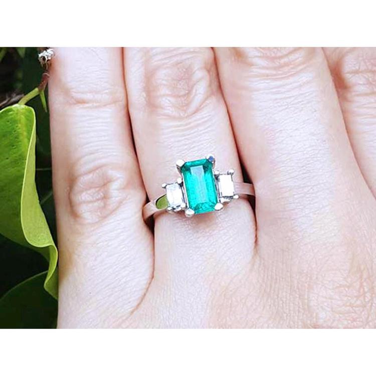A Colombian emerald engagement ring three stone with side baguette diamonds in white gold on a finger.