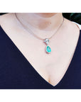 Pear-shaped emerald enhancer necklace with halo diamonds on an 18K gold chain, worn on a person.
