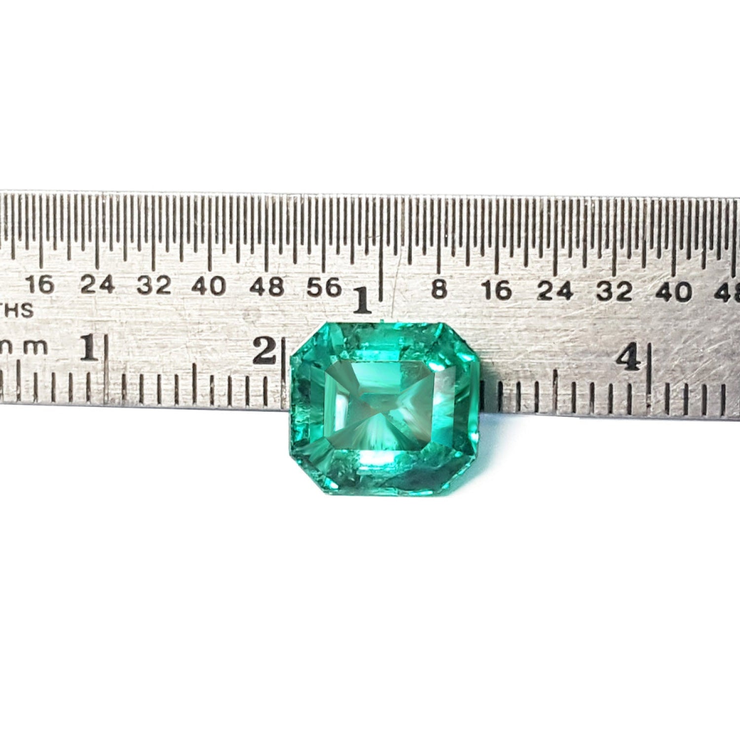 4.71 carat emerald-cut Colombian emerald, medium bluish-green, next to a ruler for scale.