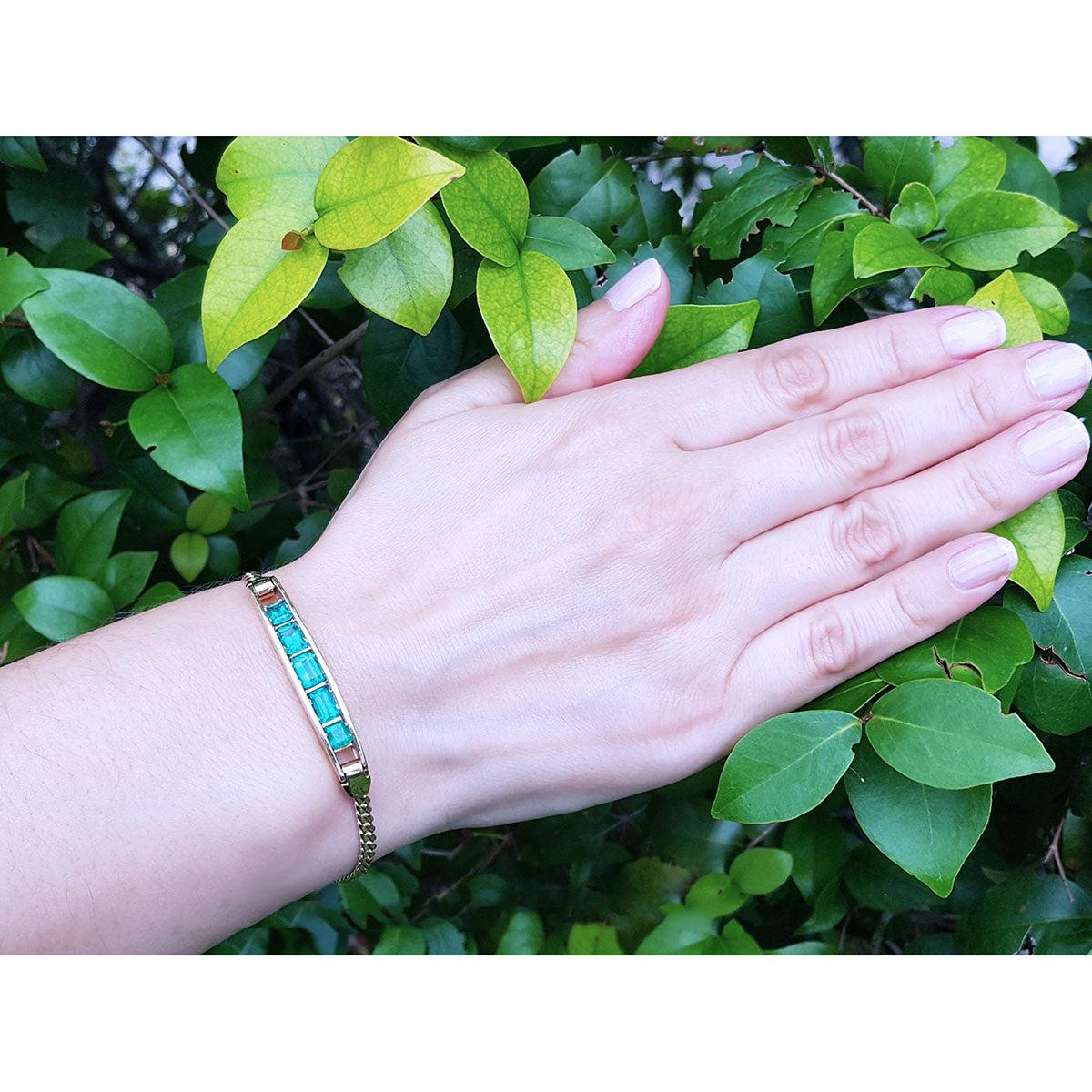 Hand wearing a colombian emerald bracelet with green leaves in the background.