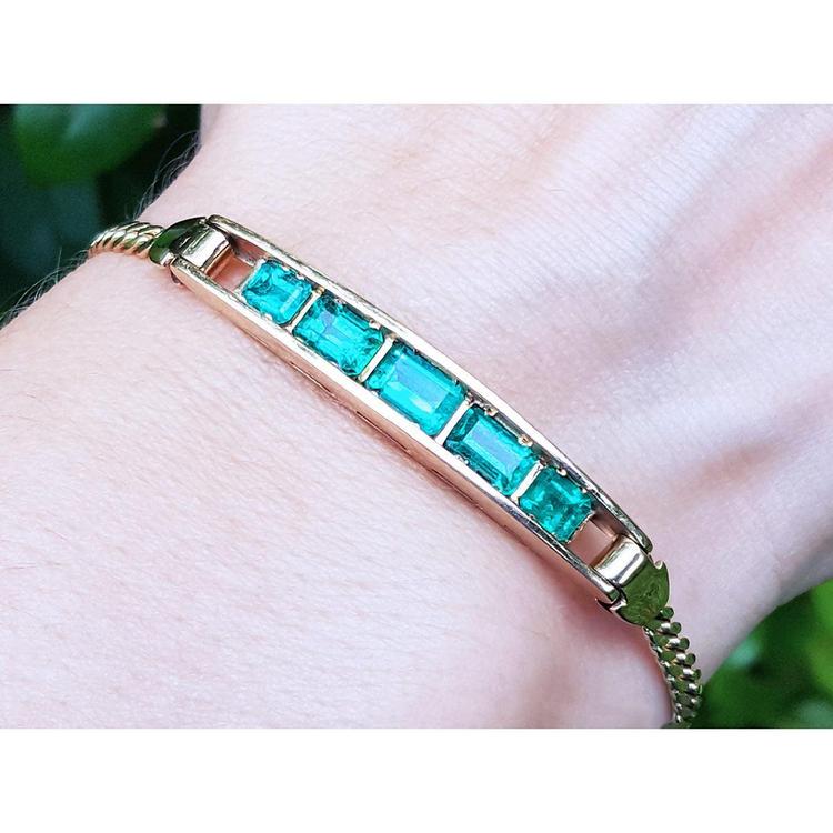 A women's emerald bracelet five premium quality Colombian Emeralds 14k Yellow Gold on a wrist.