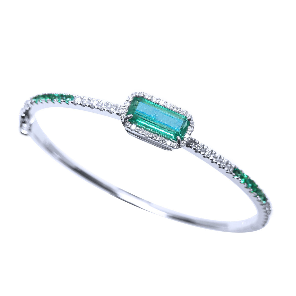On a tilted position this white gold emerald and diamond bangle bracelet shows its top and partial side profile.
