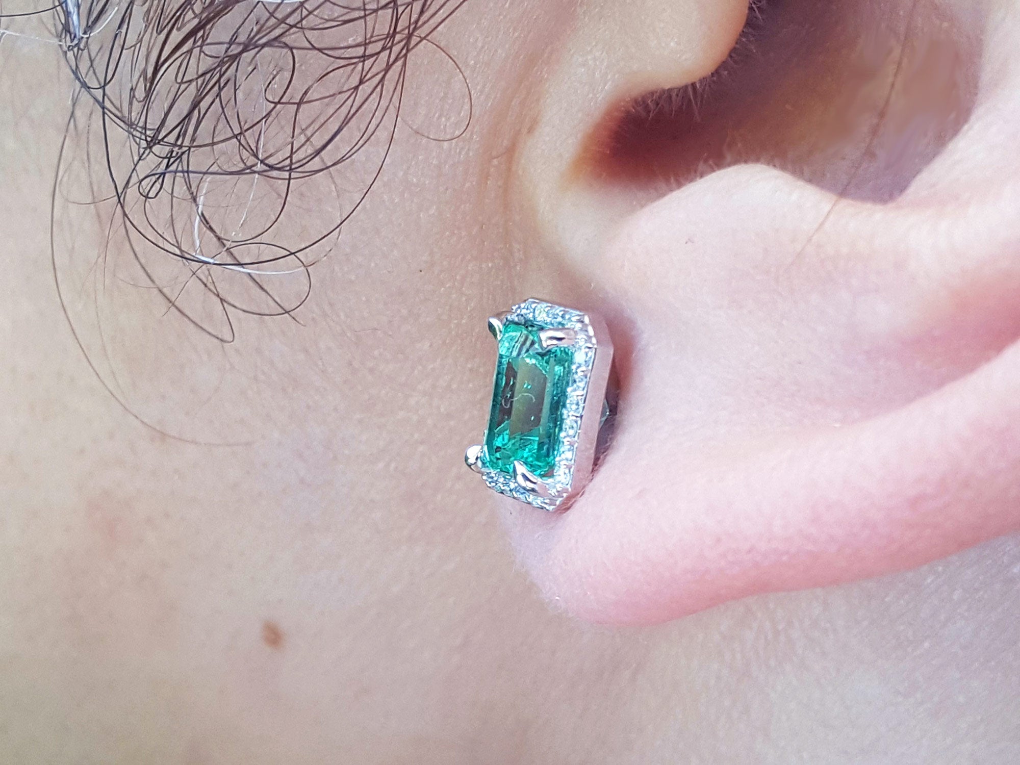 Close-up of an emerald earring left side profile on a person&#39;s ear.
