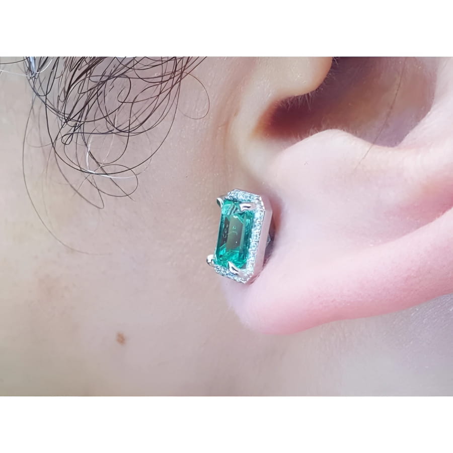 Emerald-cut natural emerald stud earring with halo diamonds in 14K white gold, worn on an ear.