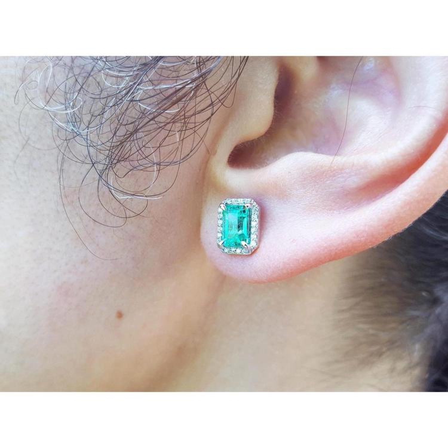 Emerald-cut natural Colombian emerald stud earring with a diamond halo, set in 14K gold on an ear.