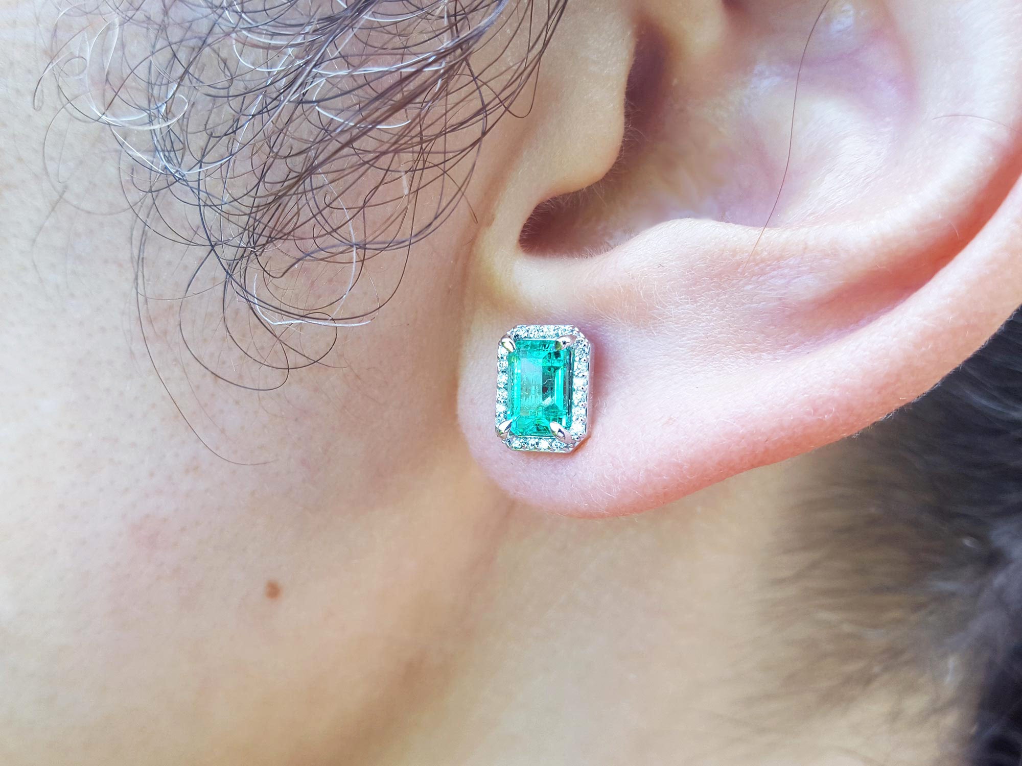 Close-up of an ear wearing a green emerald earring.