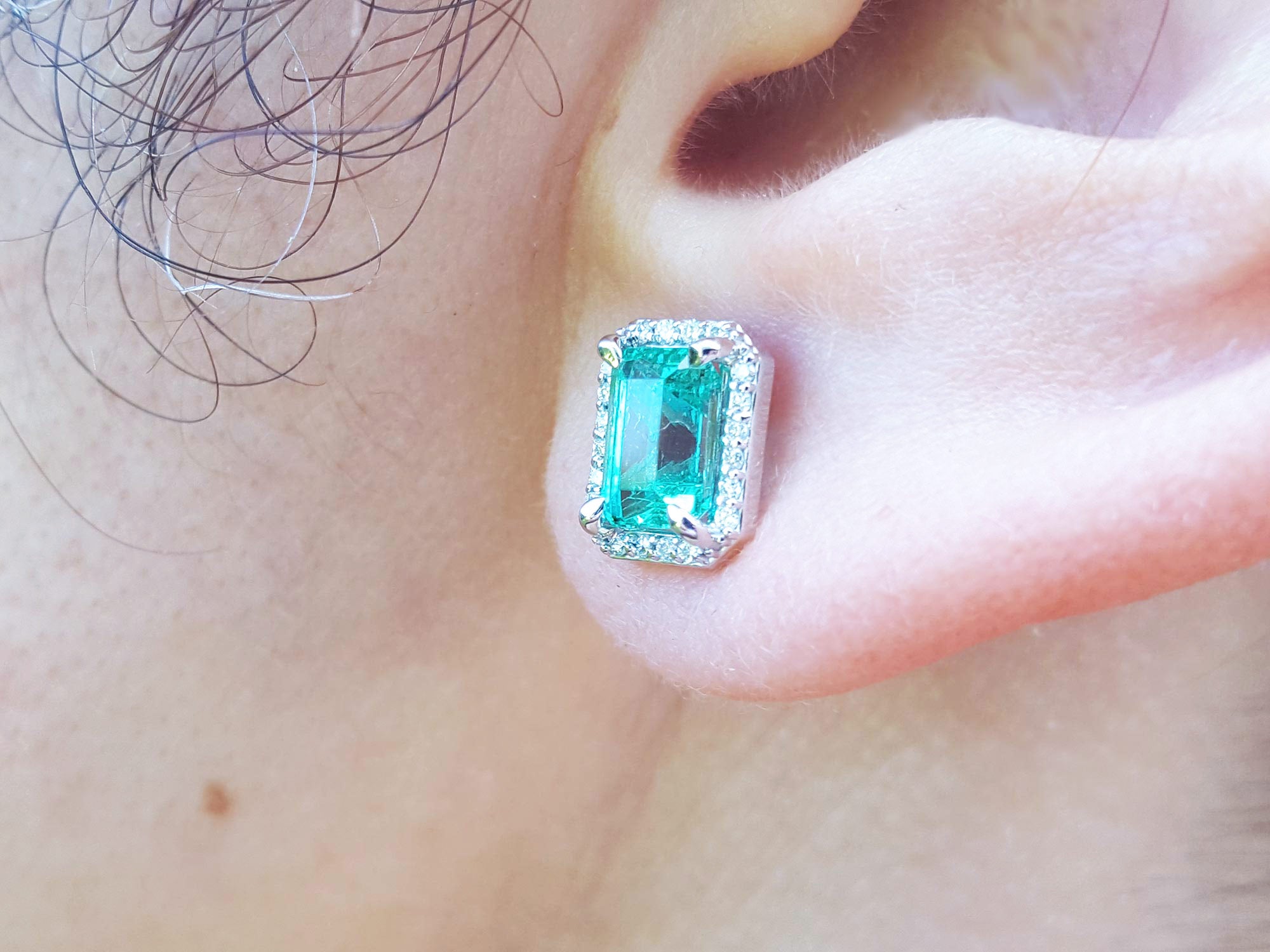 Close-up of an ear wearing a real Colombian emerald stud earring with a diamond halo.
