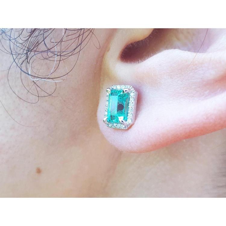 Close-up of an ear wearing a real Colombian emerald stud earring with a diamond halo.