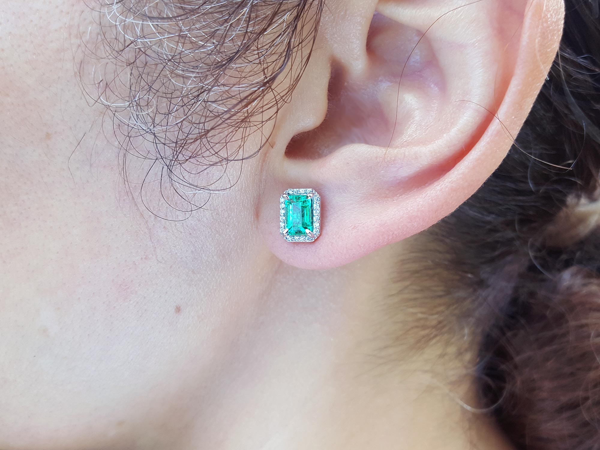 Close-up of an ear wearing a Colombian emerald earring with a white gold setting.