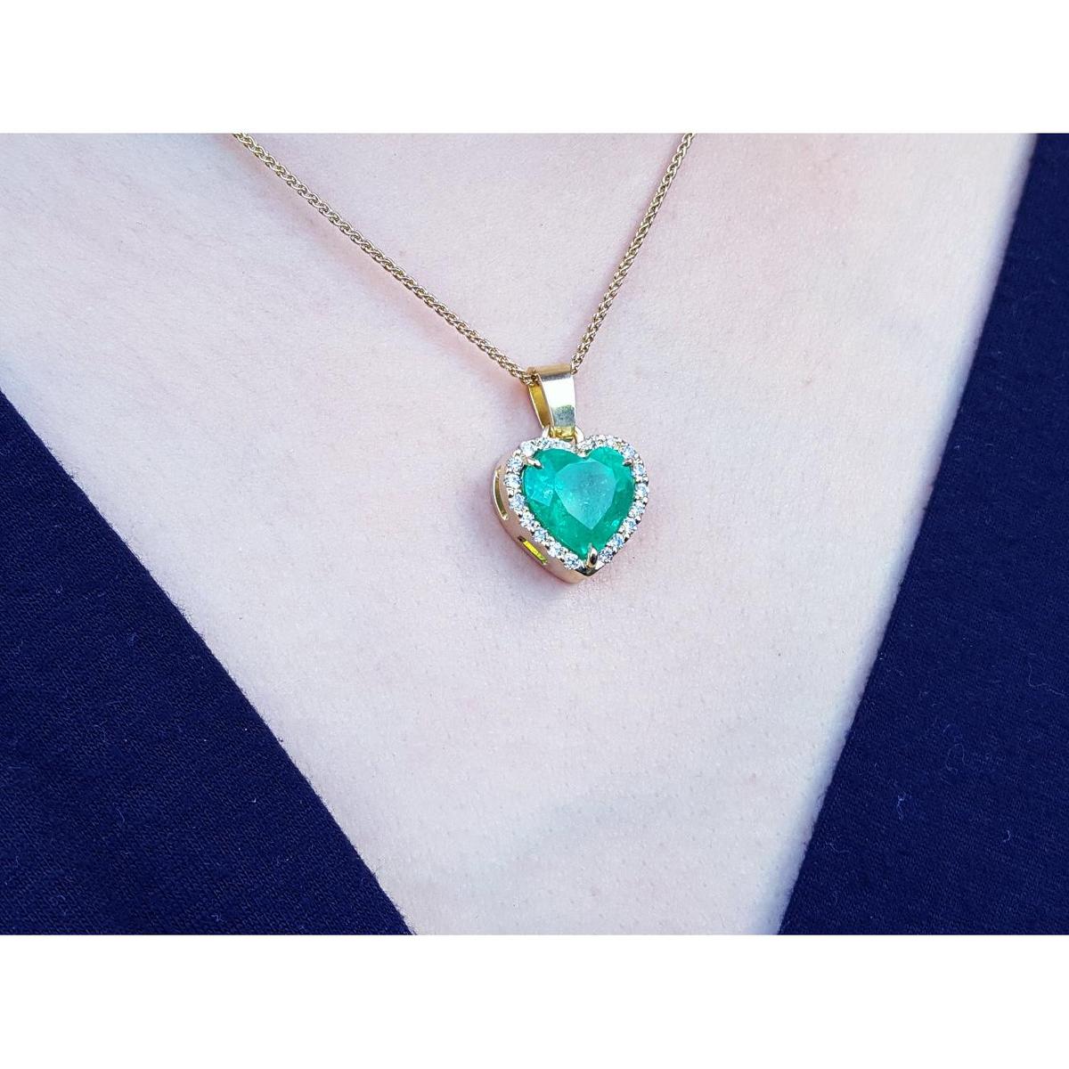 Heart-shaped emerald pendant on a gold chain against a white and blue fabric background.