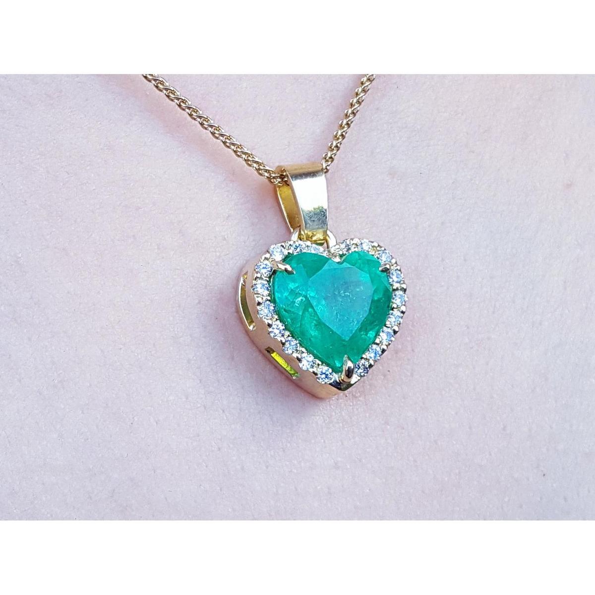 Heart-shaped emerald pendant with gold frame and diamonds on a light pink skin background.