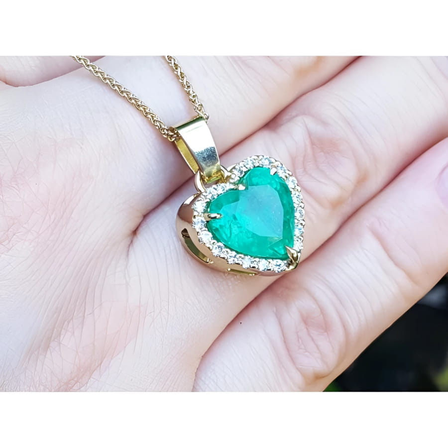 5.04 ct. heart-shaped emerald pendant with diamond halo in 18K yellow gold on a hand.