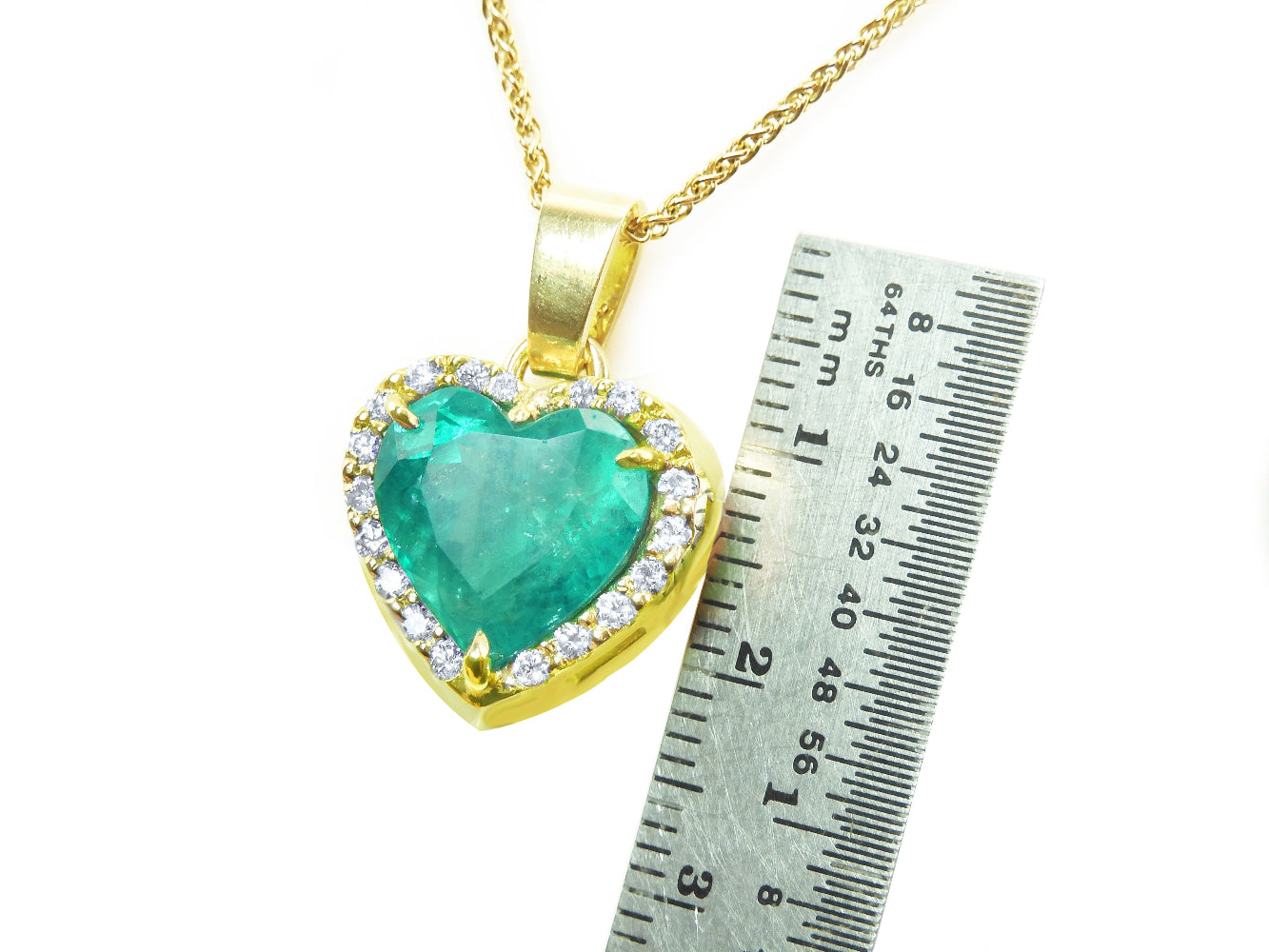 Gold pendant with a heart-shaped natural emerald and diamonds, next to a ruler for scale.