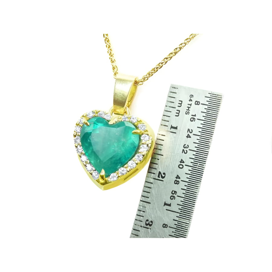 Emerald heart pendant with diamond halo in 18K yellow gold, next to a ruler for scale.