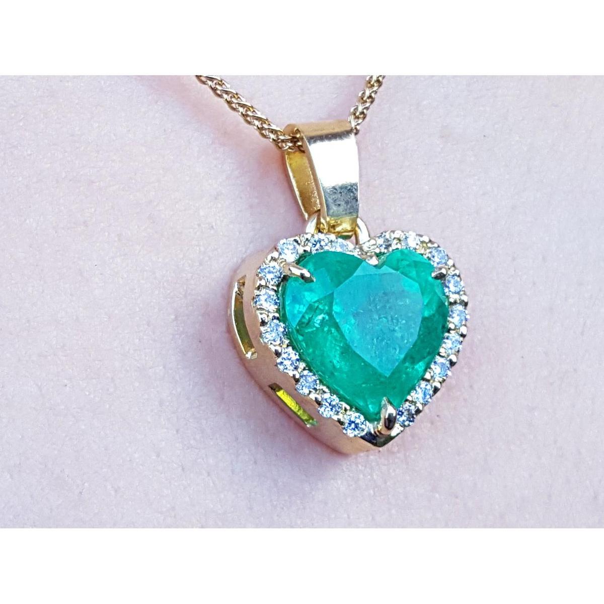 Heart-shaped emerald pendant with gold frame and diamonds on a light pink background.