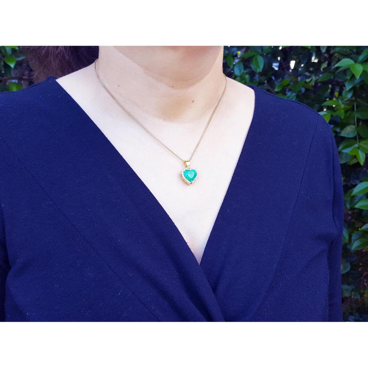 A woman wearing a blue top with a necklace featuring a natural colombian emerald heart pendant.