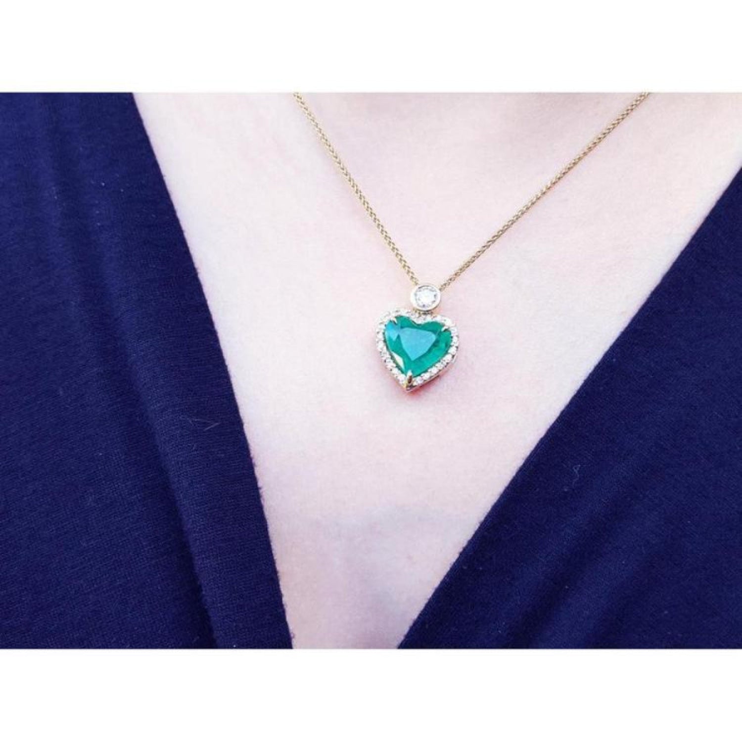 Emerald heart pendant with diamond halo on an 18k gold chain, worn on a dark top.
