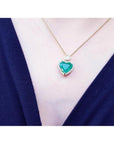 Emerald heart pendant with diamond halo on an 18k gold chain, worn on a dark top.