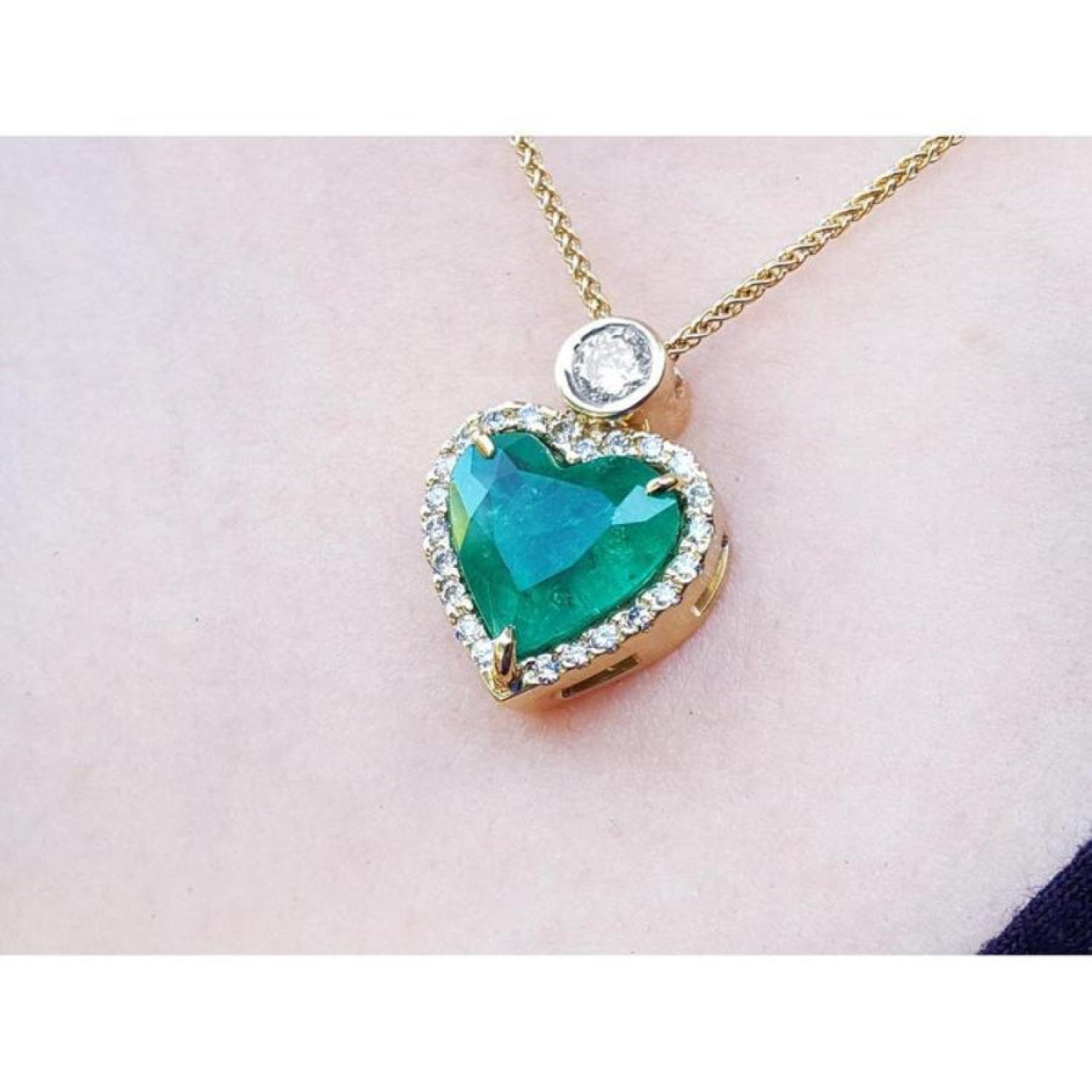 Heart-shaped Muzo colombian emerald pendant with gold chain on a light pink background.