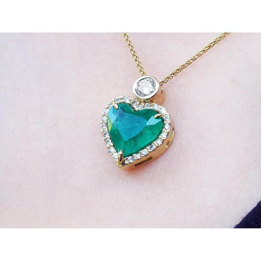 Heart-shaped Muzo colombian emerald pendant with gold chain on a light pink background.