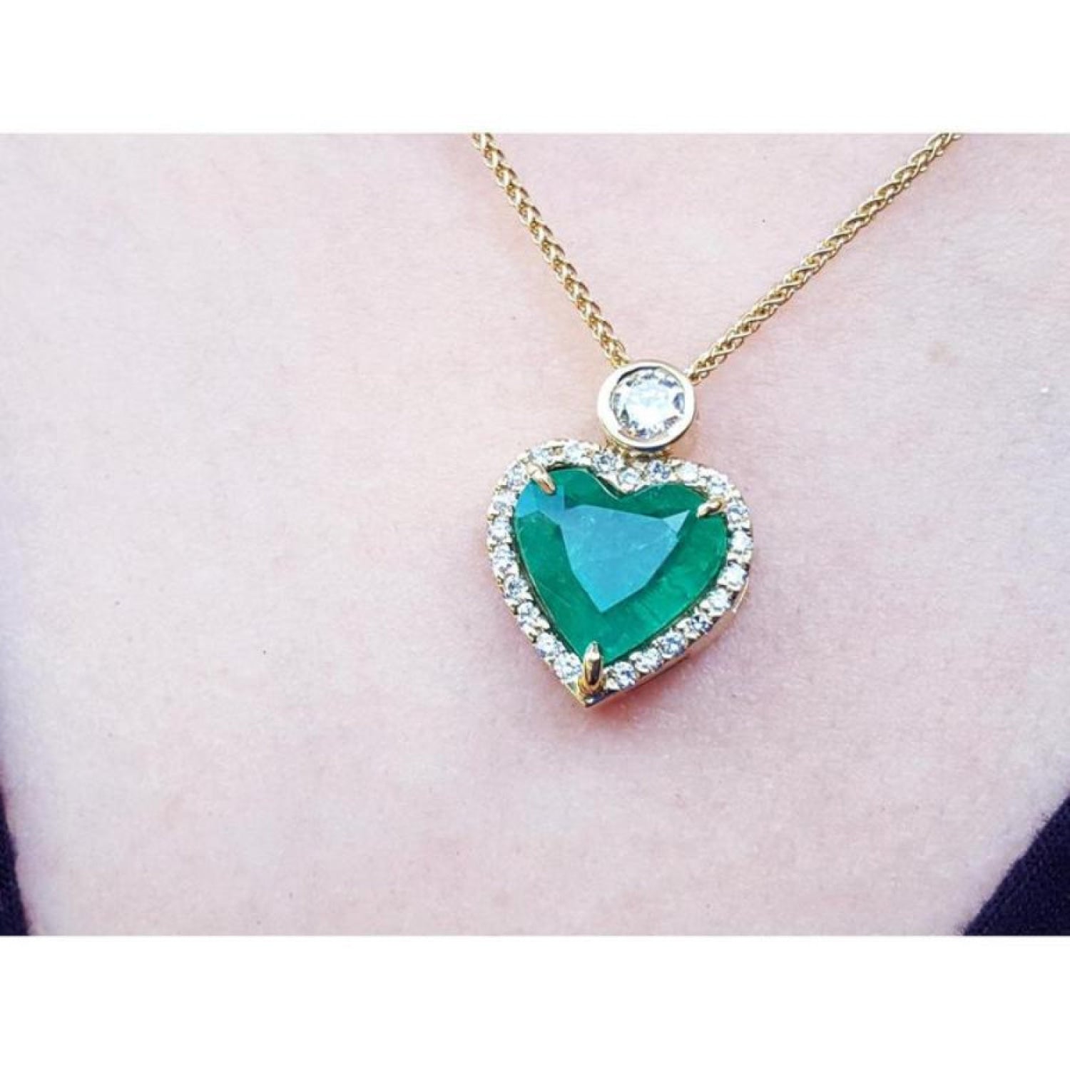 Heart-shaped emerald pendant with diamond halo and round diamond accent on an 18k gold chain.