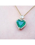 Heart-shaped emerald pendant with diamond halo and round diamond accent on an 18k gold chain.