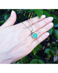 Emerald heart pendant with halo diamonds in 18K yellow gold on a hand.