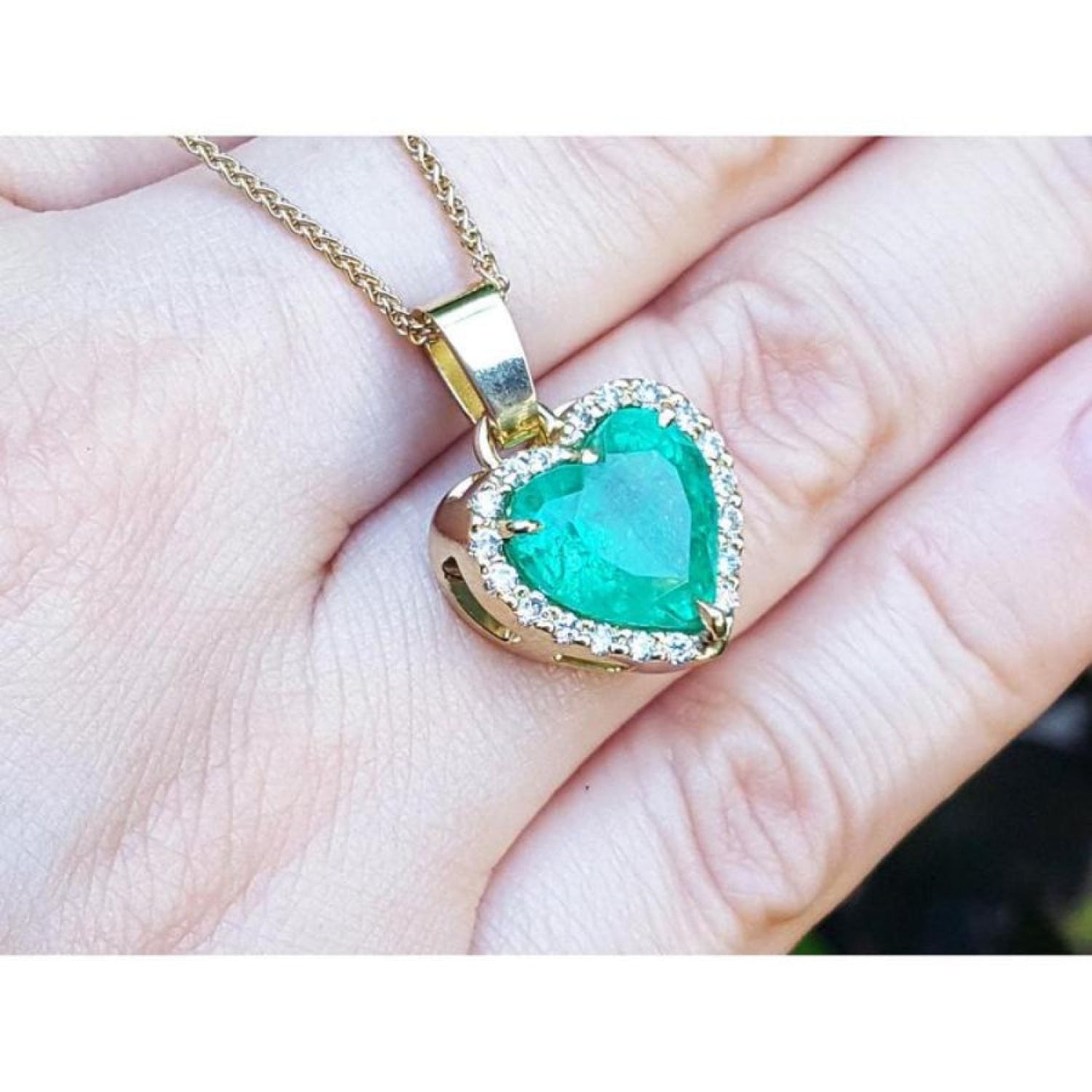 5.04 ct. heart-shaped emerald pendant with diamond halo in 18K yellow gold on a hand.