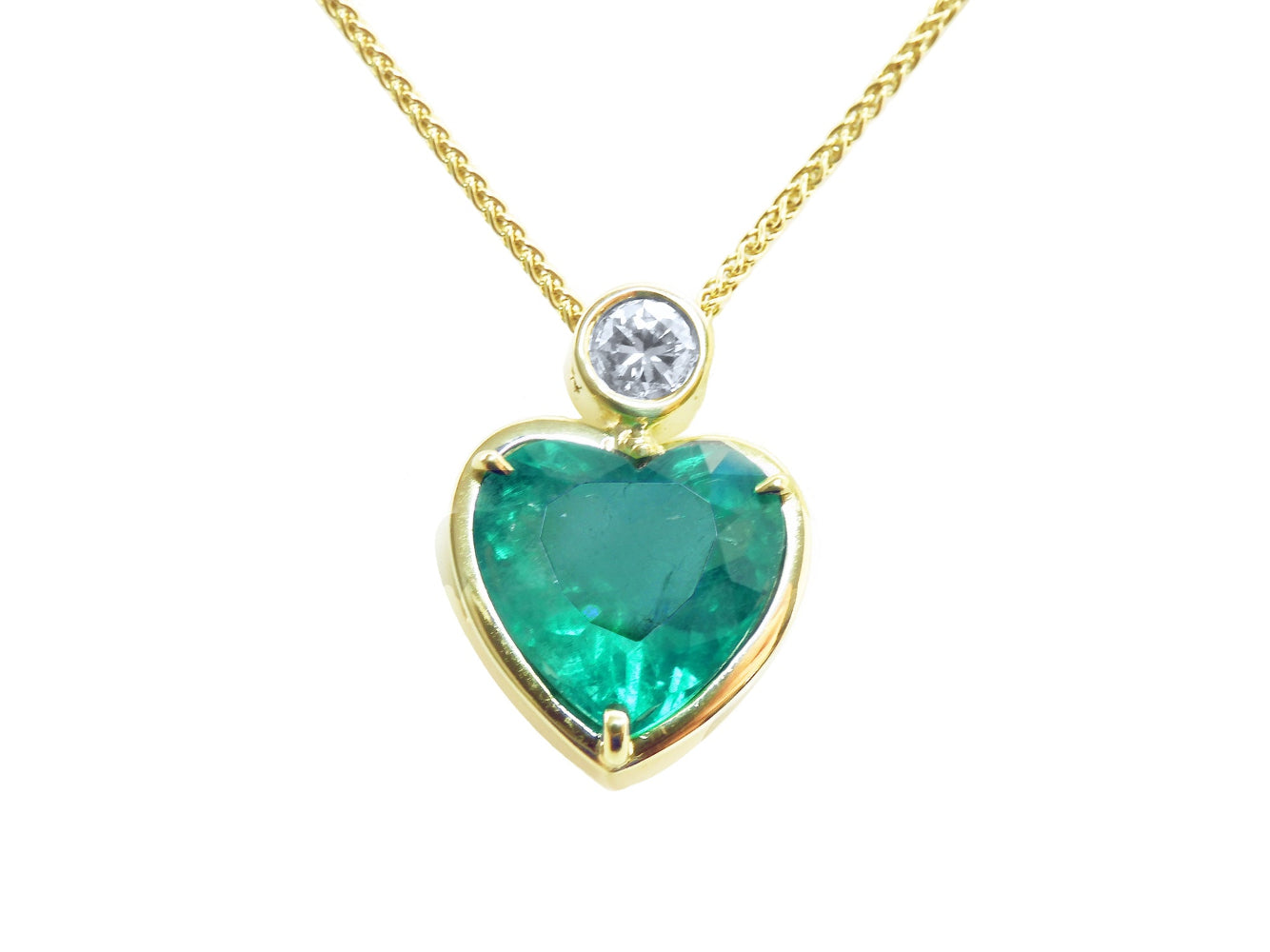 Heart-shaped emerald pendant with gold frame and diamond on a topside view.