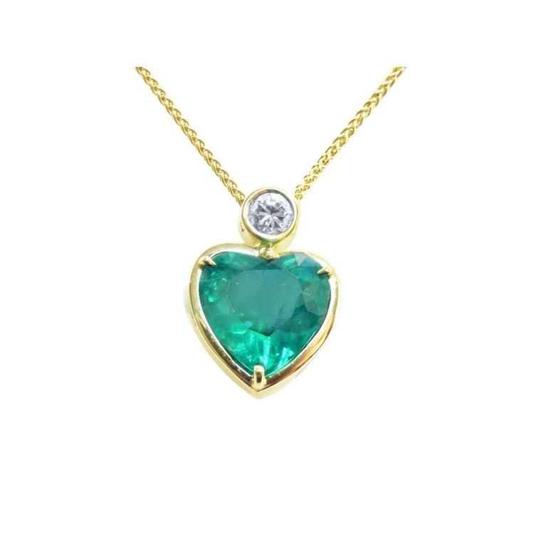 Heart-shaped emerald pendant with gold frame and diamond on a topside view.