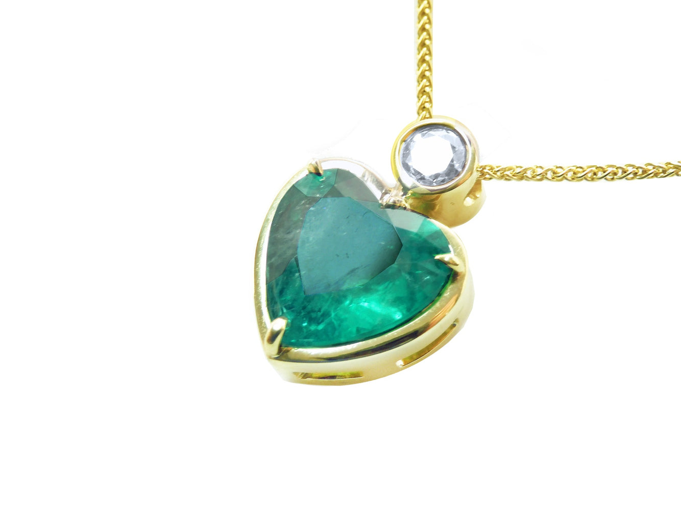 Gold pendant with a heart-shaped emerald and small diamond on top, lef-side profile view.