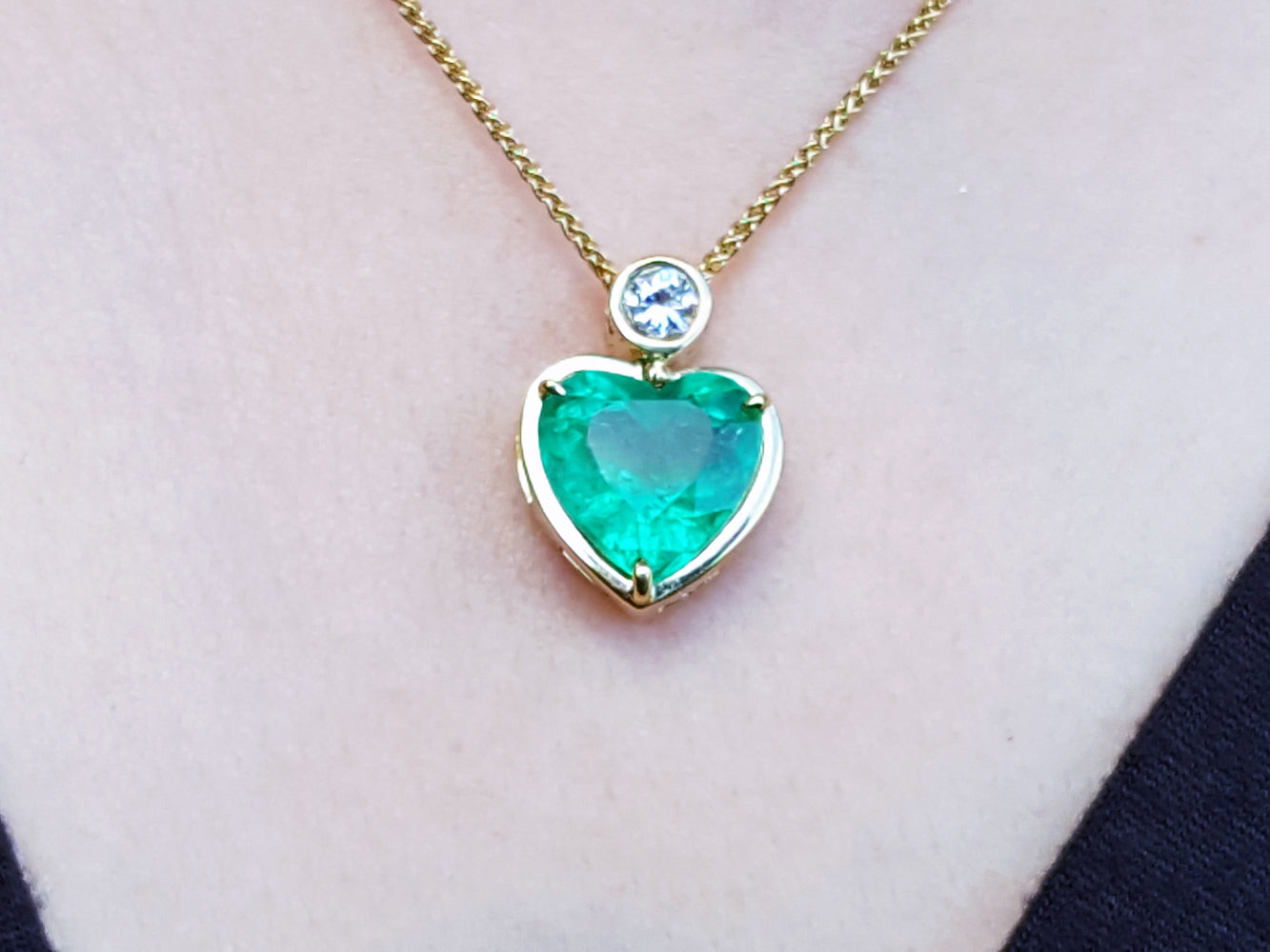 Heart-shaped emerald pendant necklace on a person&#39;s neck against a neutral background.