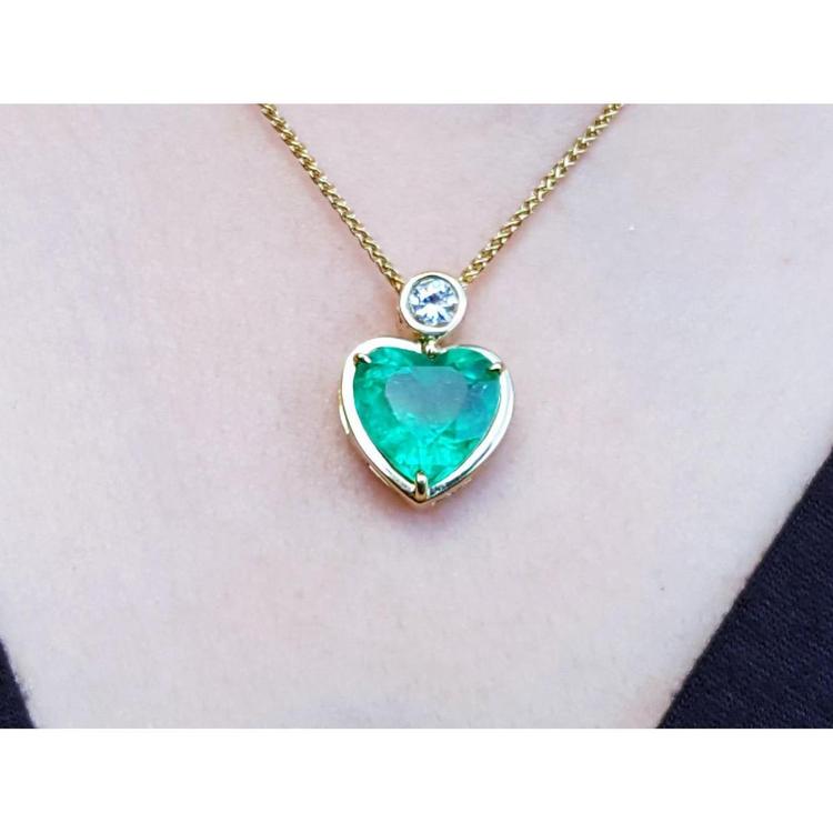 Heart-shaped emerald pendant necklace with a bezel-set diamond on an 18K yellow gold chain.