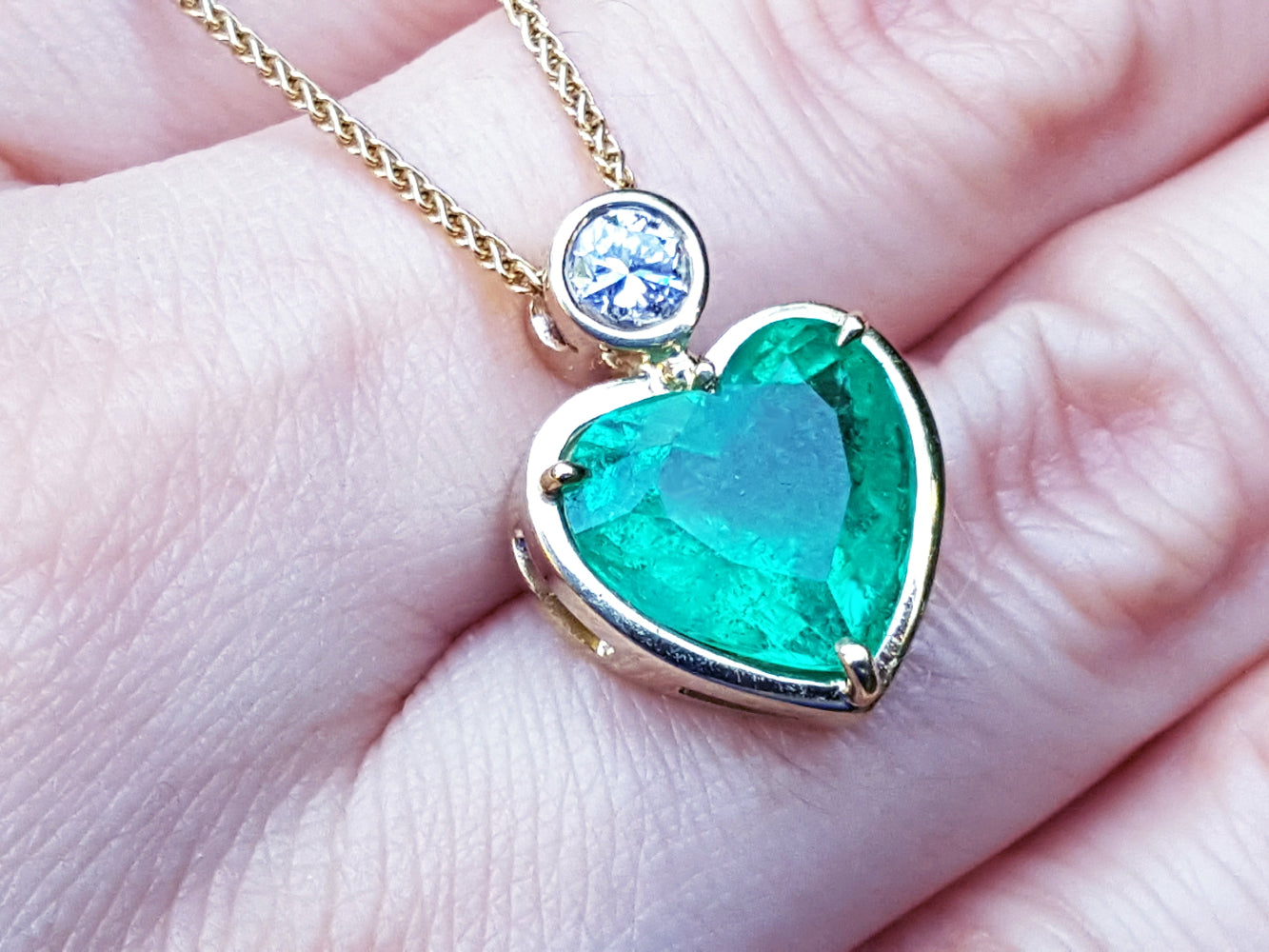 Heart-shaped emerald pendant with gold frame on a person&#39;s fingers.