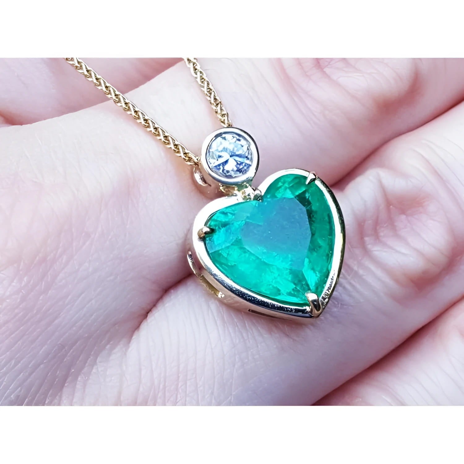 5.46 ct. heart-shaped emerald pendant in 18K yellow gold with a slider bail and bezel-set diamond.