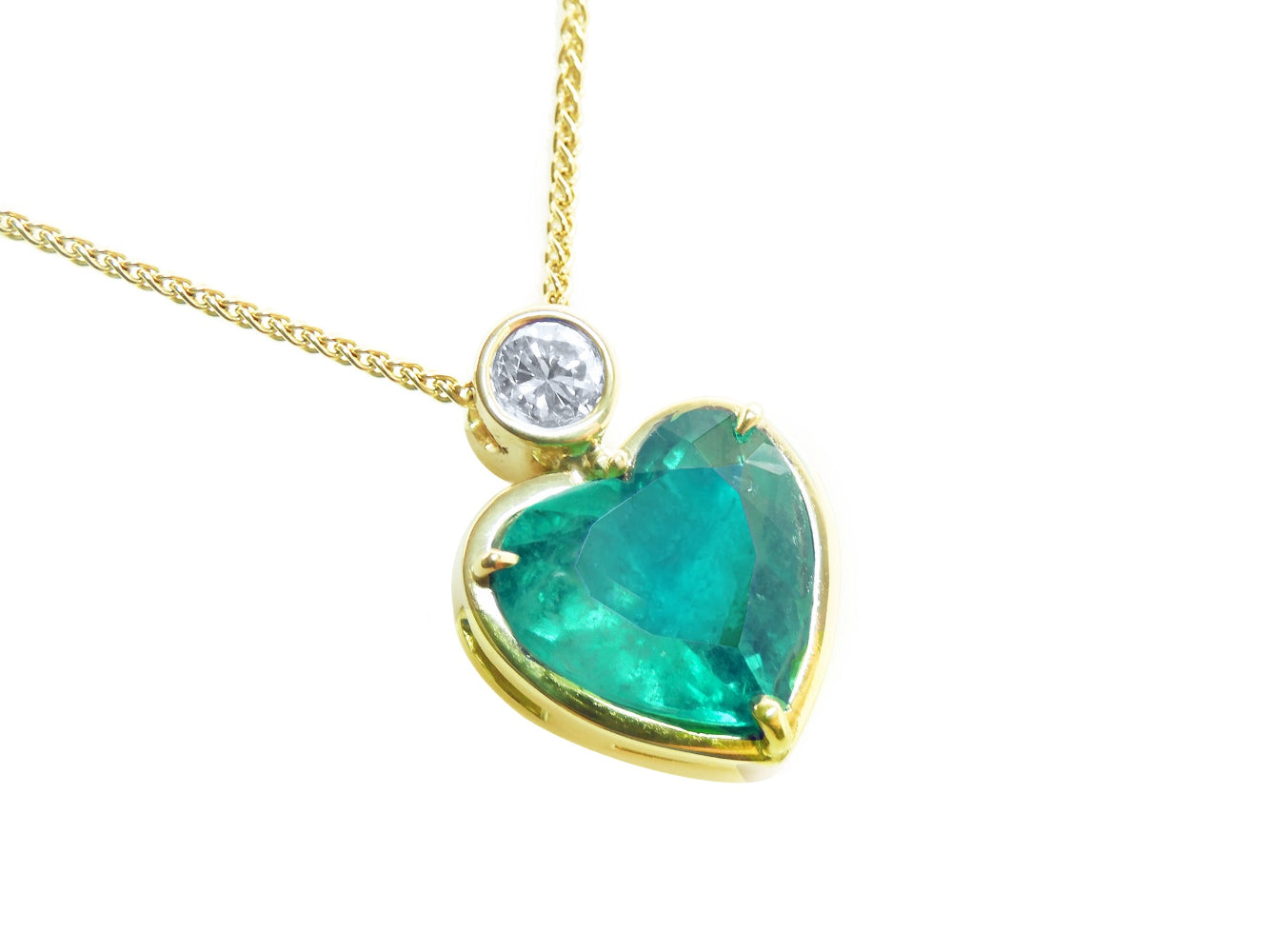 Heart-shaped emerald pendant with gold frame and diamond on a white background